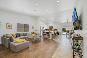 A spacious living area with a sofa, ottoman, and dining table. - NEWLY Renovated! Beautiful 4 Bedroom House! BIG Backyard! POOL / SPA ! (Desert Hot Springs)