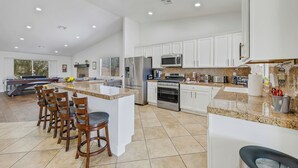 A spacious kitchen with white cabinets, granite countertops, and a central island with bar stools.