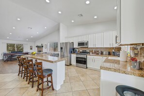 A spacious kitchen with white cabinets, granite countertops, and a central island with bar stools. - NEWLY Renovated! Beautiful 4 Bedroom House! BIG Backyard! POOL / SPA ! (Desert Hot Springs)