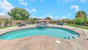 A swimming pool with a hot tub, lounge chairs, and a covered area with a tiled roof.