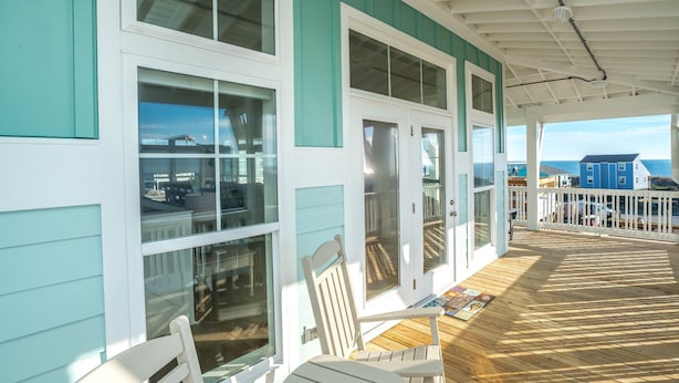 A covered porch with a wooden deck, white railings, and a view of the ocean.