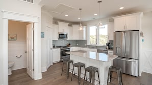 A modern kitchen with white cabinetry, stainless steel appliances, and a central island with bar stools.
