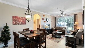 A spacious living room with a large window, a dining area with a wooden table and chairs, and a cozy seating area with a sofa and armchair. - Spacious 3 bedroom, 2 bathroom condo in a great community! (Kissimmee)
