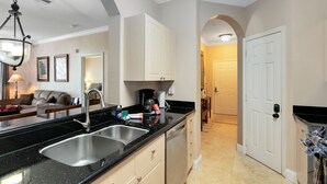 A modern kitchen with a black countertop, stainless steel sink, and white cabinets. - Spacious 3 bedroom, 2 bathroom condo in a great community! (Kissimmee)