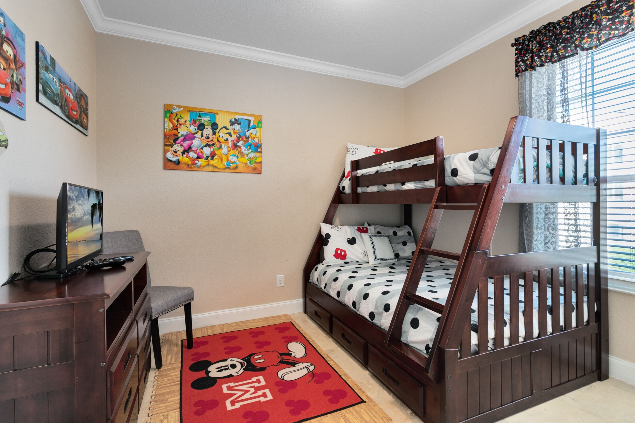 A child's bedroom with bunk beds, a desk, a chair, and a Mickey Mouse rug.