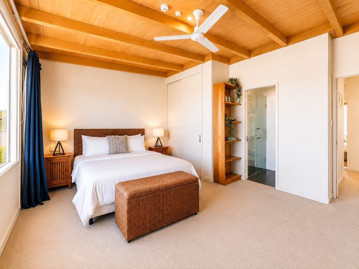 A bedroom with a bed, bedside lamps, a ceiling fan, a wooden bench, and a glass door leading to a bathroom.
