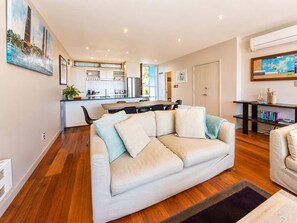 A modern living room with a sofa, a dining area, and a kitchen in the background.