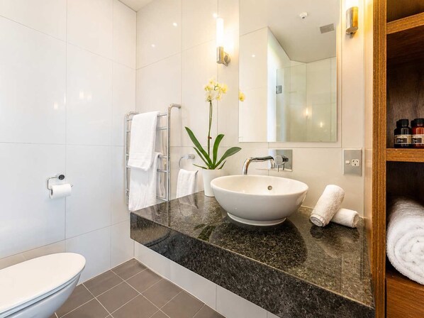 A modern bathroom with a white toilet, a sink with a marble countertop, a towel rack, and a potted plant.