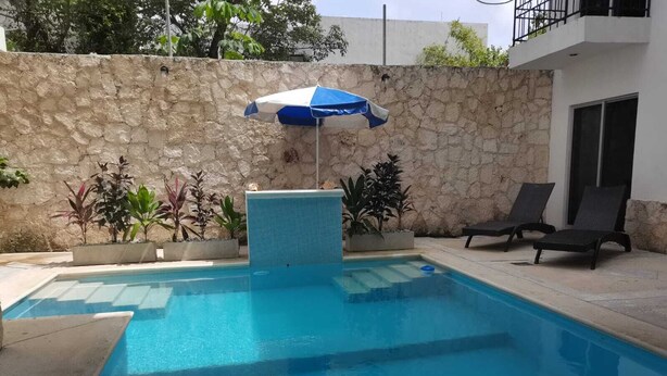 Une piscine bordée d’un muret en pierre, un parasol bleu et blanc, et deux chaises longues.
