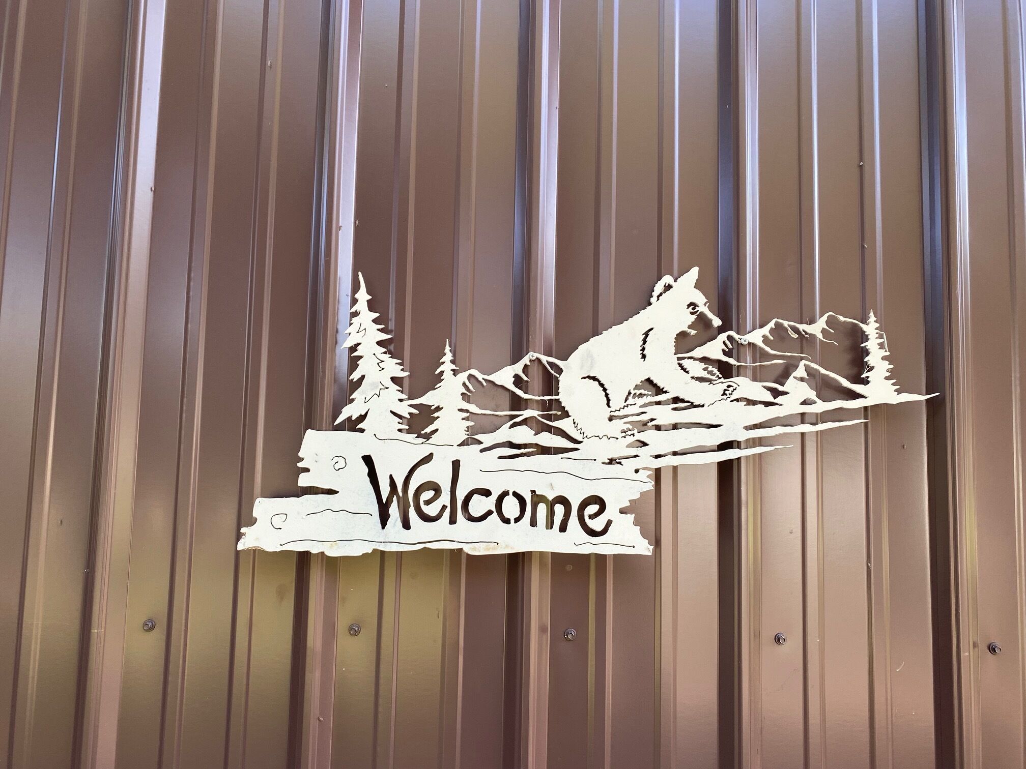 A wooden sign with a mountain and tree silhouette, and the word "Welcome" on a corrugated metal wall.