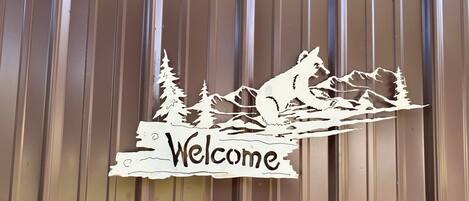 A wooden sign with a mountain and tree silhouette, and the word "Welcome" on a corrugated metal wall.