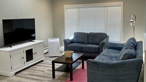 Ein modernes Wohnzimmer mit einem Flachbildfernseher, einer weißen Unterhaltungsanlage, einer grauen Sofagarnitur, einem Couchtisch und einem Deckenventilator.