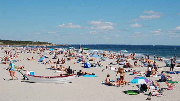 Ein überfüllter Strand mit Liegegästen, Sonnenschirmen und einem Boot.