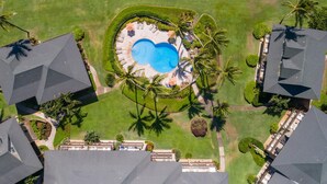 Vista aérea de un resort con una piscina central rodeada de palmeras y césped cuidado.