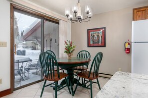 A dining area with a round table, four chairs, a chandelier, a fire extinguisher, and a framed artwork on the wall.