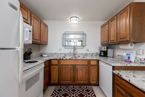 A compact kitchen with wooden cabinets, a white refrigerator, a stove, a sink, and a coffee maker. - Minutes from Whitefish & Glacier - heated pool and hot tubs (Whitefish)