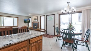 A kitchen with a marble countertop, wooden cabinets, a fireplace, and a dining area with a table and chairs.
