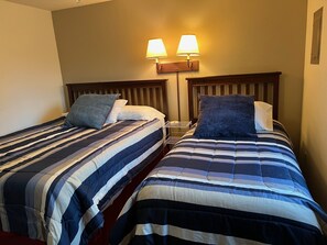 Two single beds with striped bedding, a nightstand, and two wall-mounted lamps.