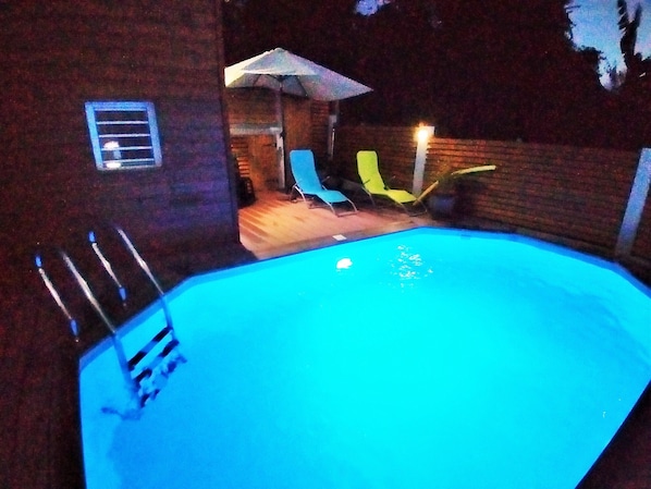 A swimming pool with a few chairs and an umbrella.