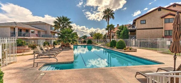 A swimming pool with lounge chairs, surrounded by residential buildings and palm trees. - Red Sands Retreat l Pool & Spa l Pets (St. George)