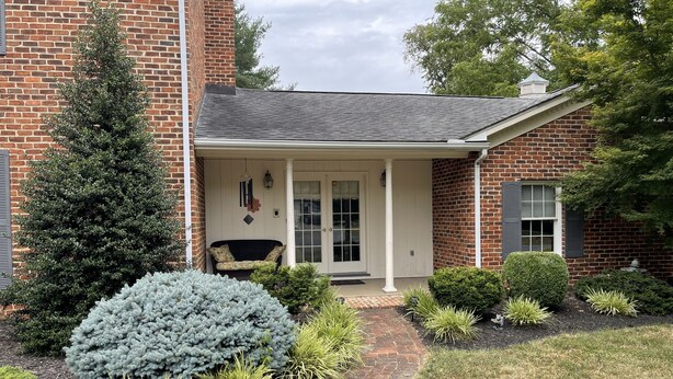 A brick house with a porch, a front door, and a small garden with various plants. - Beekeeper's House (Buena Vista)
