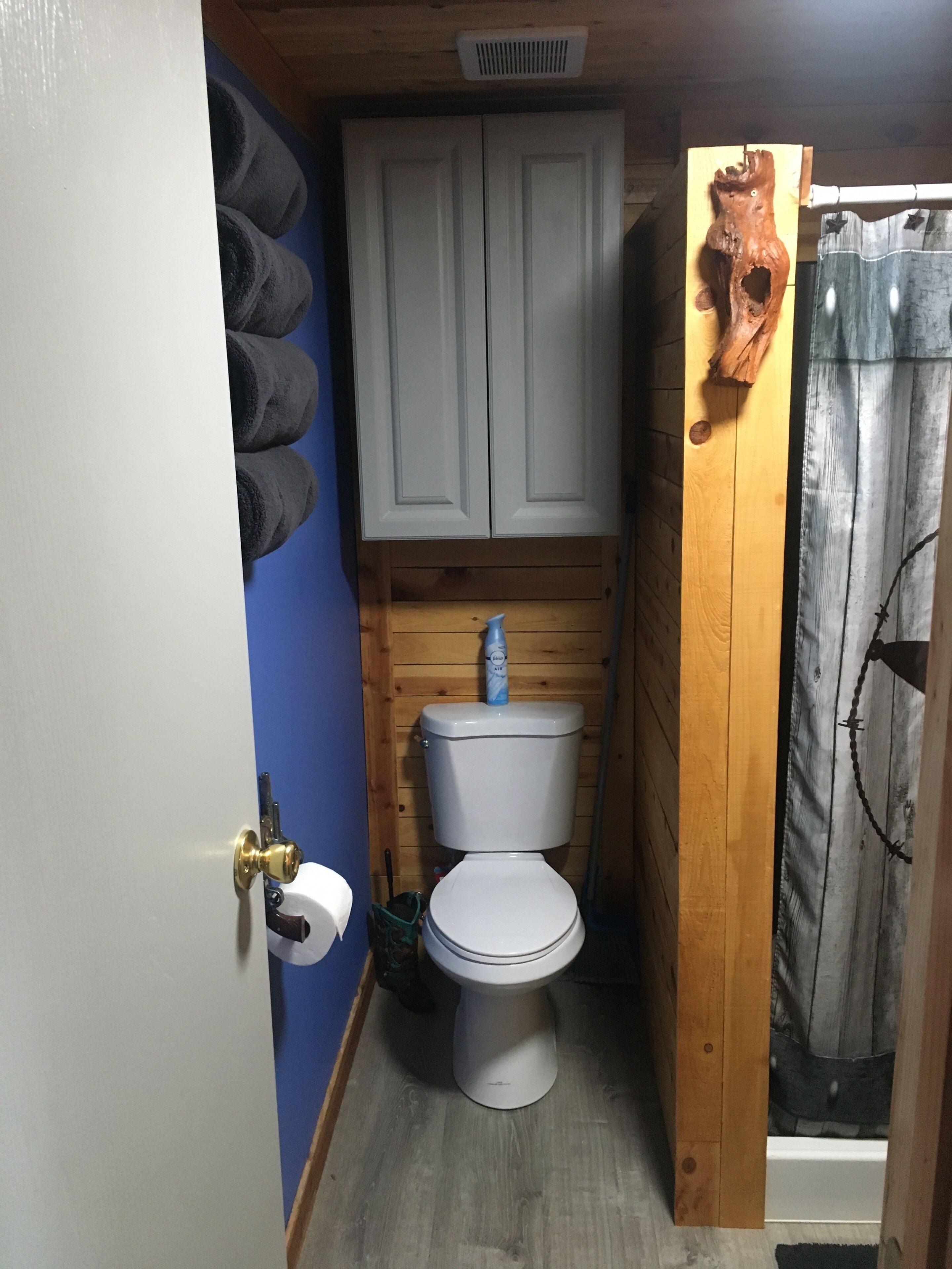 A small, compact bathroom with a white toilet, a wooden cabinet above, and a shower curtain with a branch design.