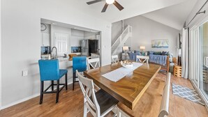 A spacious dining area with a wooden table and chairs, a ceiling fan, and a kitchen in the background.