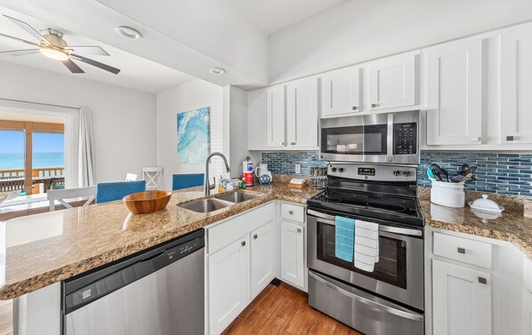 A modern kitchen with white cabinets, a granite countertop, stainless steel appliances, and a view of the ocean.