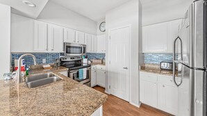 A modern kitchen with white cabinets, a granite countertop, stainless steel appliances, and a blue-tiled backsplash.