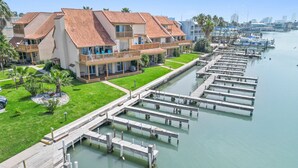 A marina with docked boats, a grassy area with palm trees, and a building with balconies.