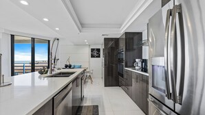 Eine moderne Küche mit einem Edelstahlkühlschrank, dunklen Schränken und einem großen Fenster mit Blick aufs Meer.