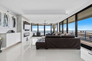 Ein modernes Wohnzimmer mit einer großen Couch, einem flachbildfernseher an der Wand und einem Balkon mit Meerblick.