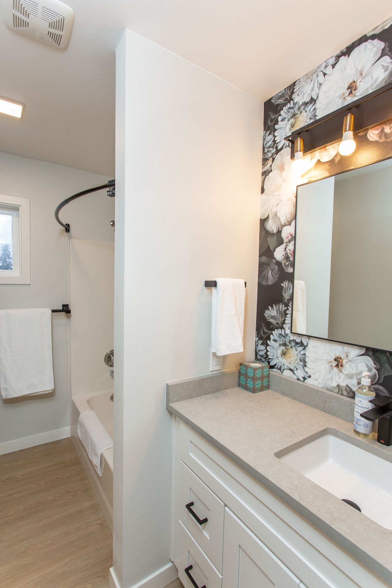 Een badkamer met een douche, twee wasbakken, een grote spiegel en bloemenbehang.