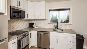 A modern kitchen with white cabinets, a stainless steel dishwasher, and a window with a view of trees. - Stunning Views from this Modern Hood Canal Retreat (Union)