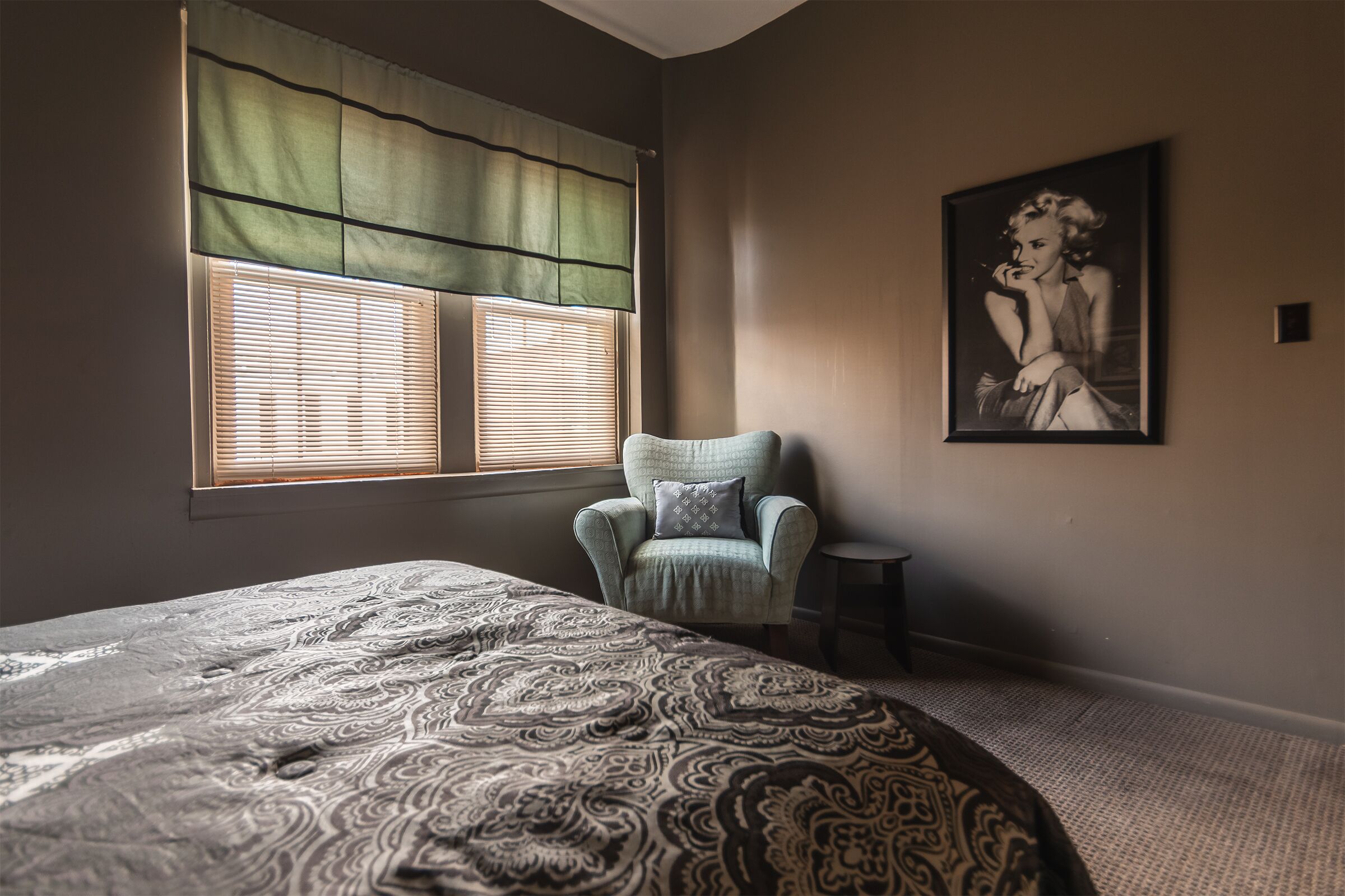 Una camera da letto con un letto grande, una sedia, una finestra con persiane e un quadro appeso al muro.