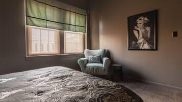 Una camera da letto con un letto grande, una sedia, una finestra con persiane e un quadro appeso al muro.