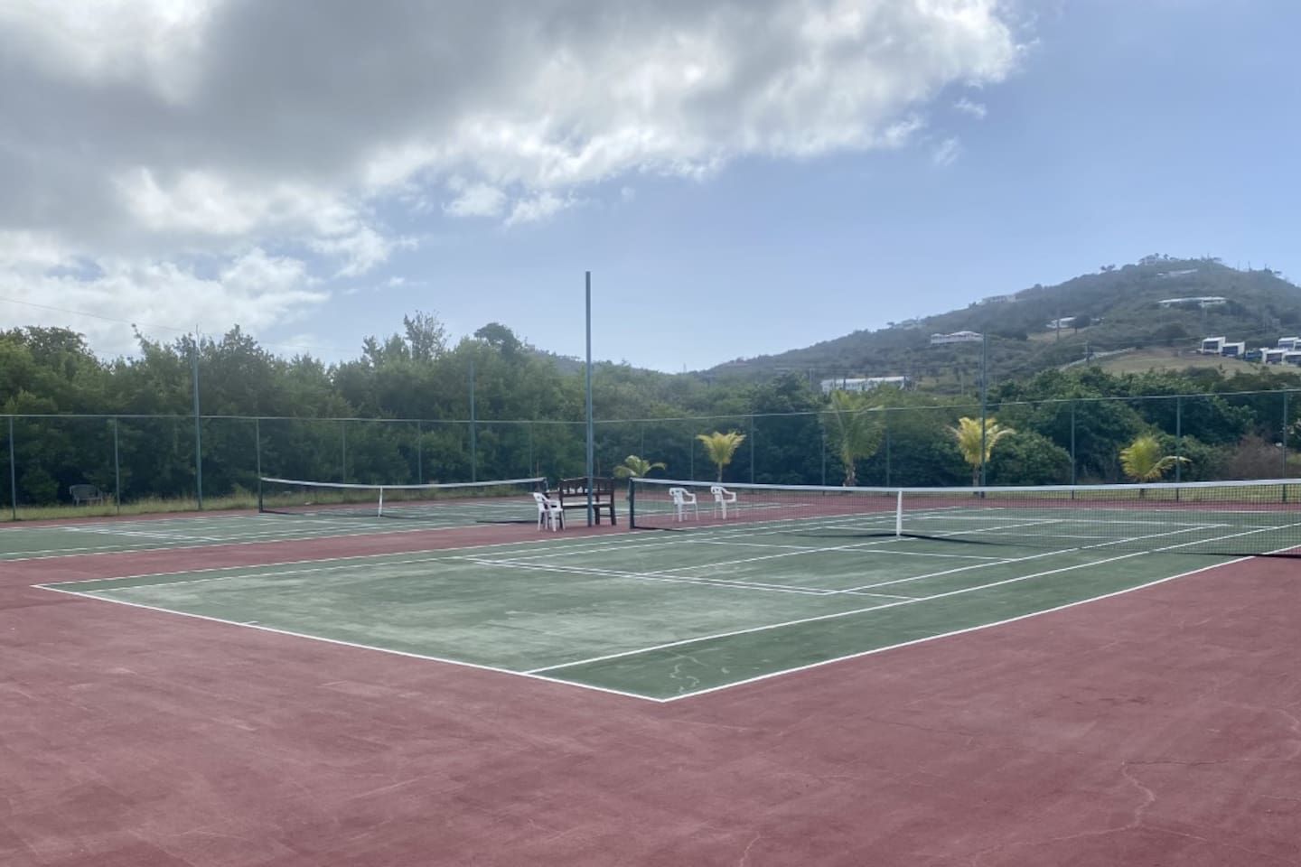Un court de tennis avec un filet, des bancs et une clôture.