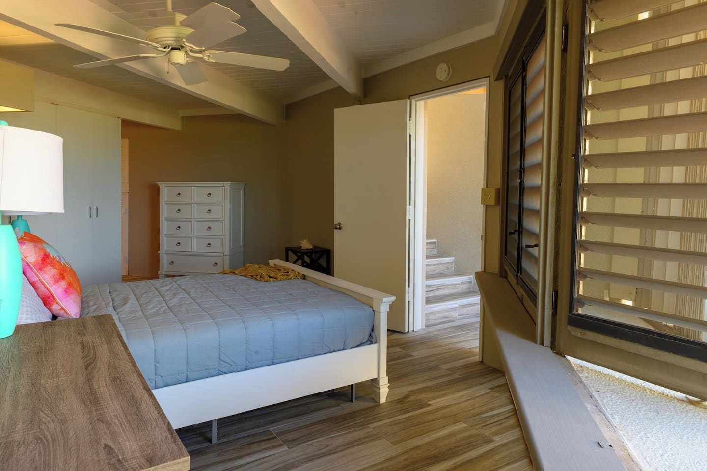 Een slaapkamer met een bed, een plafondventilator, een kaptafel en een deur naar een trap.