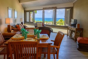 Comedor con vista al océano, muebles de madera y un televisor sobre un mueble bajo.