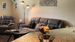 A living room with a brown leather sofa, a small round table, a floor lamp, and a decorative wall piece.
