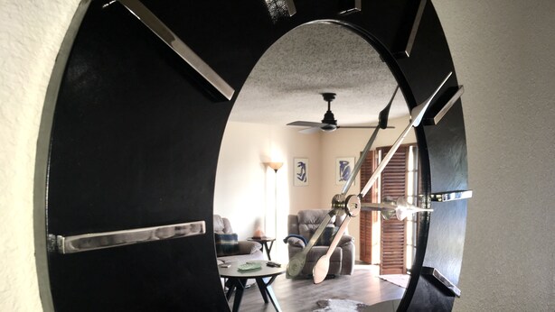 A circular mirror reflecting a living room with a ceiling fan, a sofa, and a coffee table.