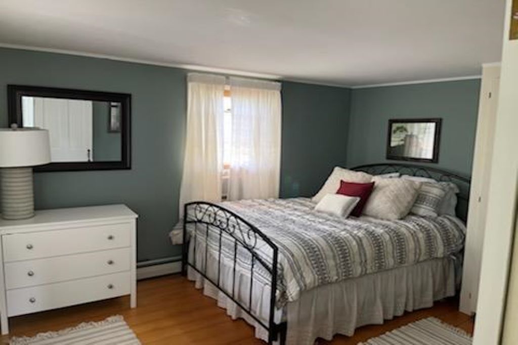 A bedroom with a bed, a nightstand, a mirror, and a window with curtains.