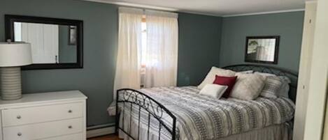 A bedroom with a bed, a nightstand, a mirror, and a window with curtains.