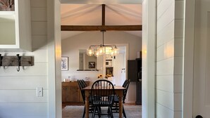 A dining area with a wooden table and chairs, a chandelier, and a view into the kitchen. - Perfect VT getaway - great for two families! Starlink Internet, Large Yard (Stratton)