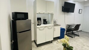 A modern kitchen with a refrigerator, microwave, and coffee maker. There is a TV mounted on the wall, a dining table with chairs, and a small potted plant. - 5 Start* New Beautiful Cozy Apart in San Juan P.R (San Juan)