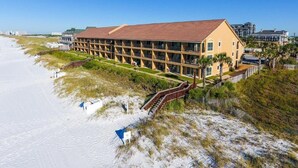 A beachfront hotel with a long, single-story structure, a covered outdoor area, and a sandy beach area. - Location Location Location!! (Destin)