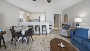 A modern living room with a dining area, a blue sofa, a coffee table, and a ceiling fan. - Location Location Location!! (Destin)