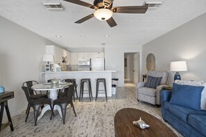 Ein modernes Wohnzimmer mit Essbereich, einem blauen Sofa, einem Couchtisch und einem Deckenventilator.
