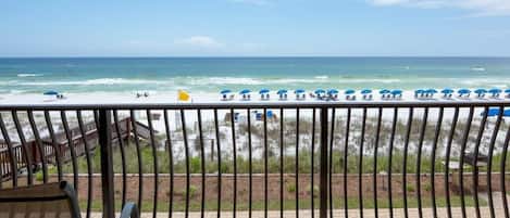A balcony with a view of the beach, including umbrellas and lounge chairs.