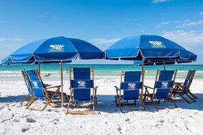 A beach with four blue beach chairs and two large blue umbrellas with the Coral Reef Club logo. - Location Location Location!! (Destin)